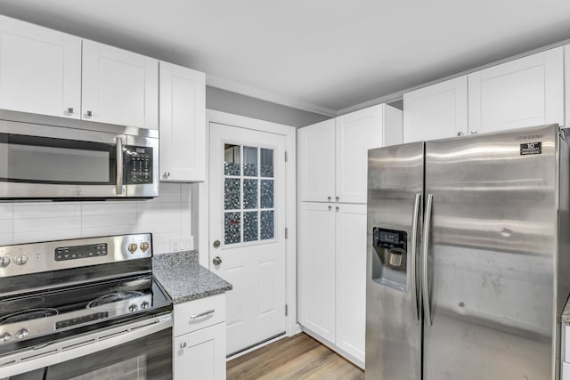 kitchen with tasteful backsplash, dark stone countertops, white cabinets, light hardwood / wood-style floors, and stainless steel appliances