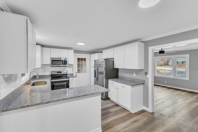 kitchen with sink, white cabinetry, stainless steel appliances, light stone counters, and kitchen peninsula