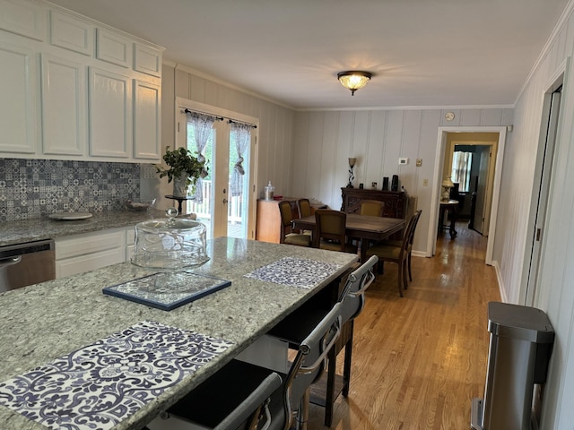 kitchen featuring white cabinetry, light stone counters, tasteful backsplash, ornamental molding, and light wood-type flooring