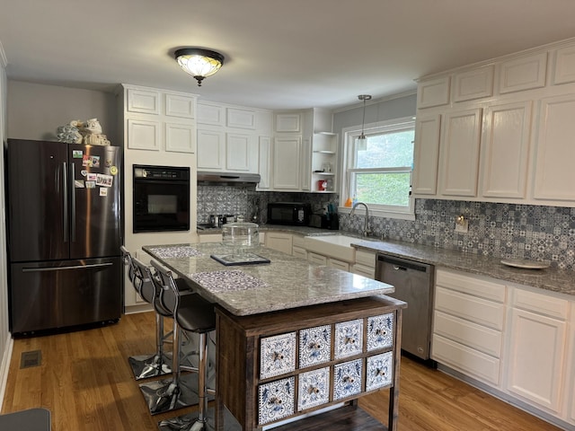 kitchen featuring decorative light fixtures, sink, white cabinets, a center island, and black appliances