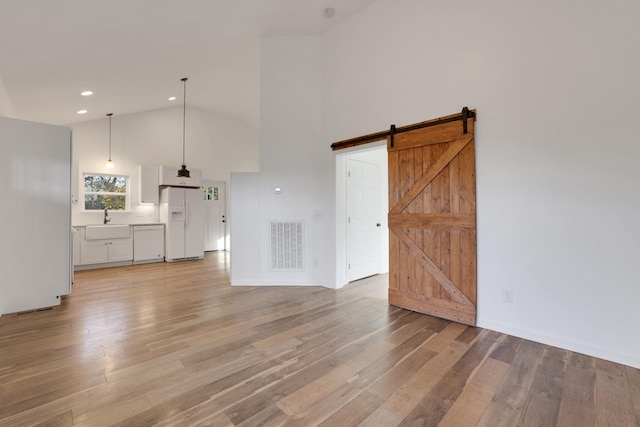 unfurnished living room with a barn door, sink, high vaulted ceiling, and light hardwood / wood-style flooring