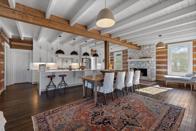 dining area with a stone fireplace, dark wood-type flooring, sink, and beam ceiling