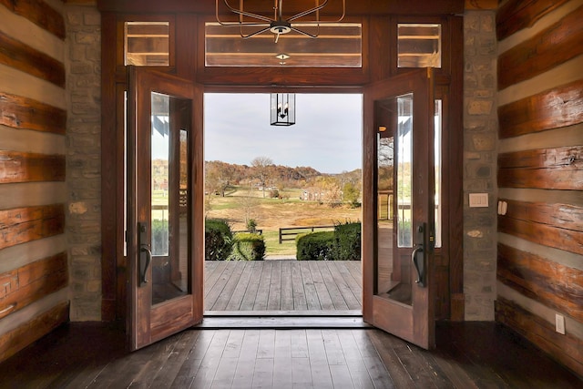 doorway to outside featuring dark wood-type flooring, a notable chandelier, wooden walls, and french doors