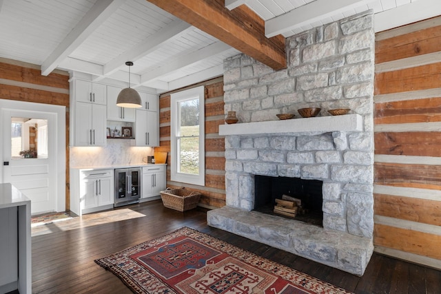 living room with dark wood-type flooring, wooden walls, wine cooler, a stone fireplace, and beamed ceiling