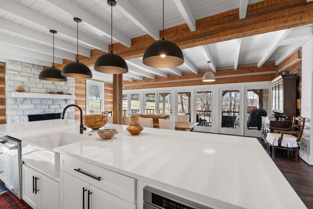 kitchen featuring pendant lighting, sink, white cabinetry, a fireplace, and beamed ceiling