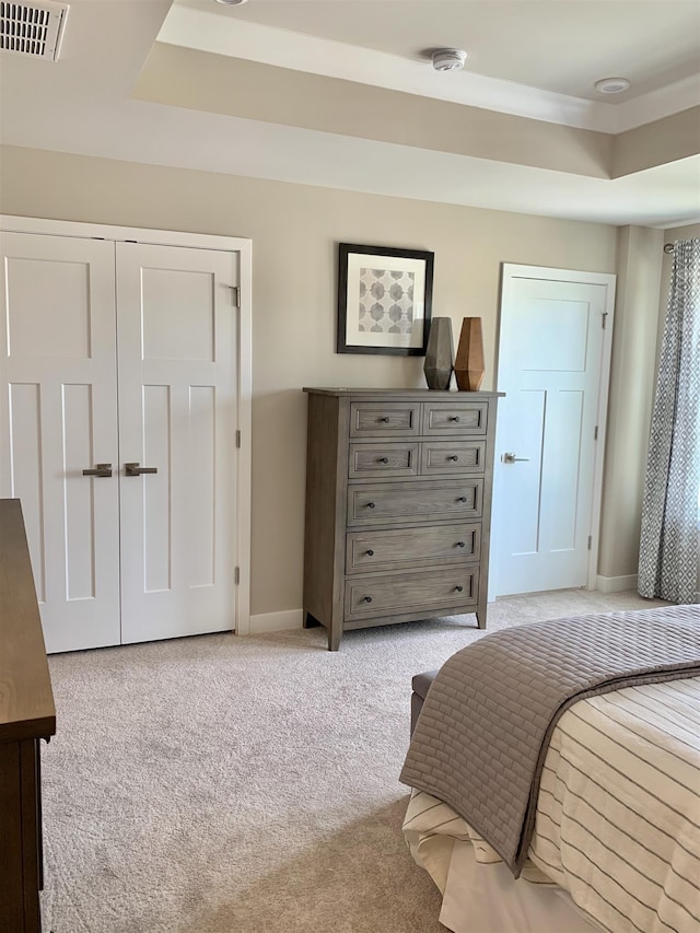 carpeted bedroom featuring a raised ceiling and a closet