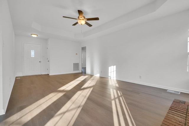 unfurnished living room with a raised ceiling, hardwood / wood-style flooring, and ceiling fan