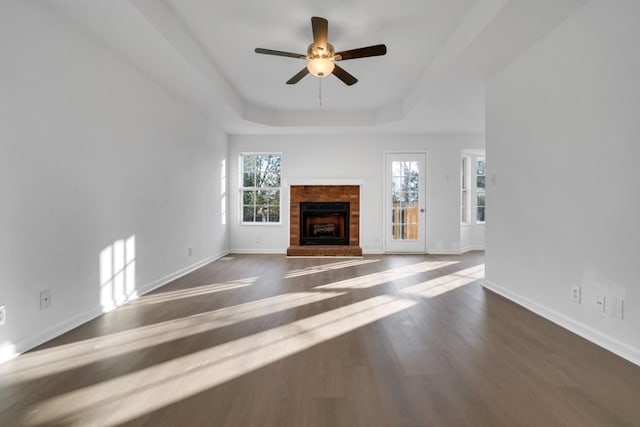 unfurnished living room with ceiling fan, dark hardwood / wood-style floors, a fireplace, and a tray ceiling