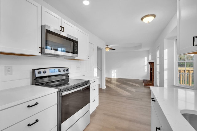 kitchen with ceiling fan, white cabinetry, stainless steel appliances, light stone counters, and light wood-type flooring