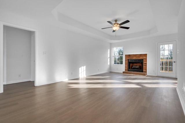 unfurnished living room with dark hardwood / wood-style floors, a healthy amount of sunlight, a tray ceiling, and a brick fireplace