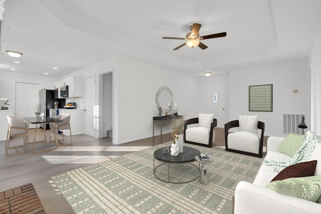 living room with a tray ceiling, ceiling fan, and light wood-type flooring