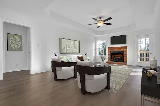 living room featuring dark hardwood / wood-style floors, a fireplace, a tray ceiling, and a wealth of natural light