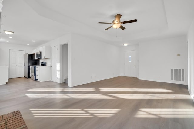 unfurnished living room with ceiling fan, light wood-type flooring, and a tray ceiling