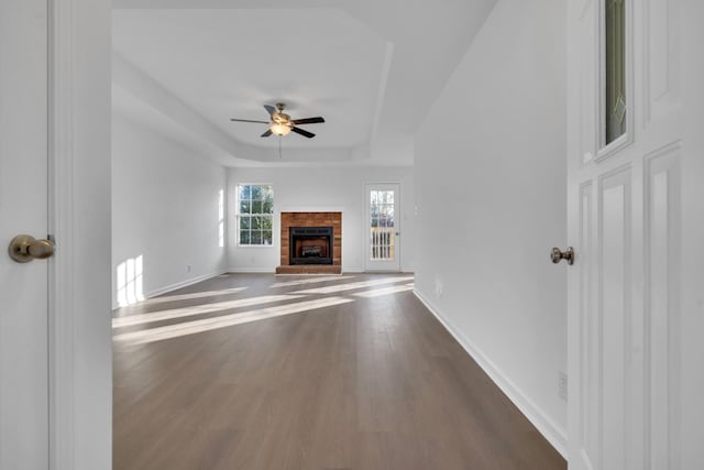 unfurnished living room with ceiling fan, a fireplace, dark hardwood / wood-style flooring, and a tray ceiling