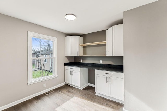 kitchen featuring white cabinetry, built in desk, and light wood-type flooring