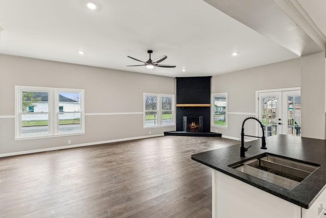 kitchen featuring french doors, sink, a brick fireplace, a center island with sink, and hardwood / wood-style floors