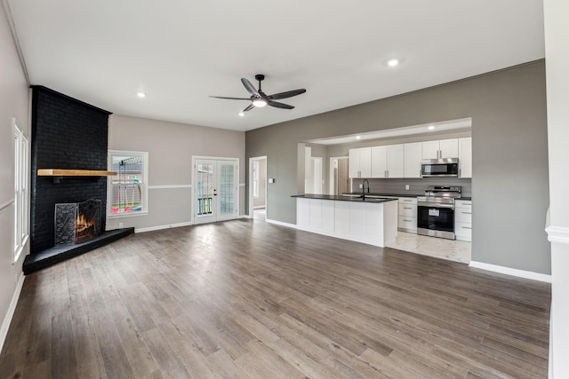 unfurnished living room with a brick fireplace, sink, ceiling fan, and light wood-type flooring