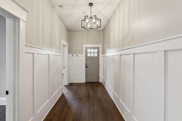 doorway with ornamental molding, dark hardwood / wood-style floors, and a notable chandelier