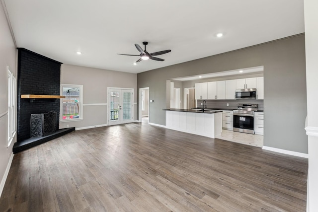 unfurnished living room with french doors, sink, a brick fireplace, light hardwood / wood-style flooring, and ceiling fan