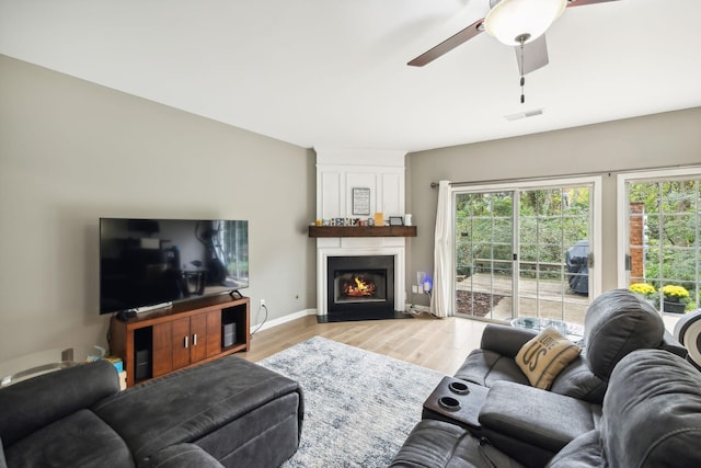 living room featuring a healthy amount of sunlight, a large fireplace, ceiling fan, and light wood-type flooring