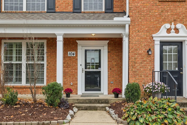 doorway to property featuring brick siding and a shingled roof