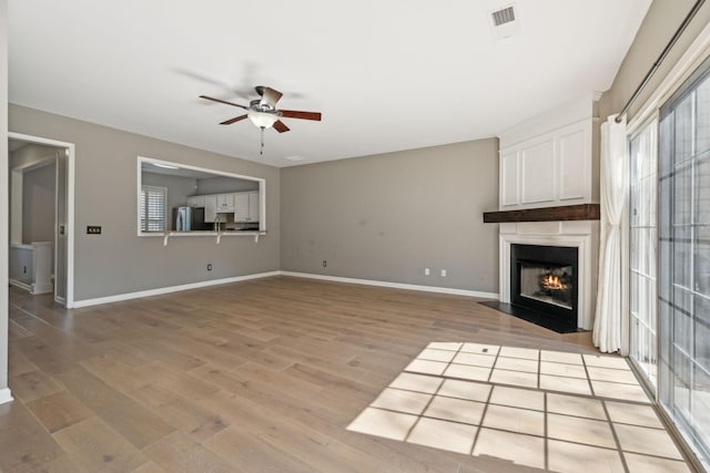 unfurnished living room with visible vents, a large fireplace, baseboards, light wood-type flooring, and a ceiling fan