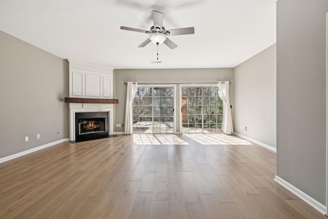 unfurnished living room with ceiling fan, a large fireplace, baseboards, and wood finished floors