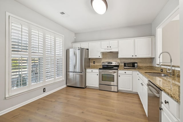 kitchen with light wood finished floors, visible vents, under cabinet range hood, stainless steel appliances, and a sink