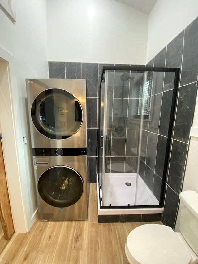 bathroom with walk in shower, stacked washer / dryer, toilet, and hardwood / wood-style floors