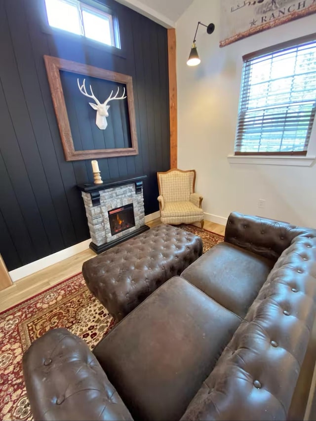 living room featuring a stone fireplace, hardwood / wood-style floors, and wooden walls