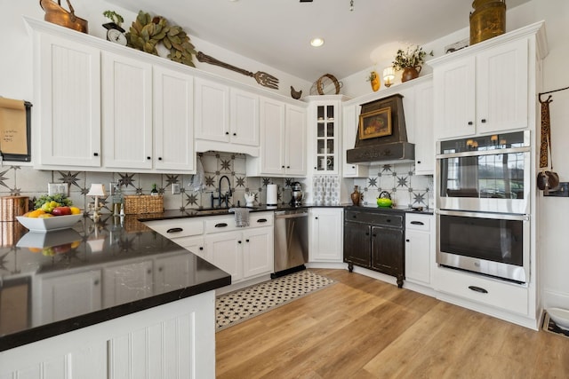 kitchen with sink, appliances with stainless steel finishes, white cabinetry, light hardwood / wood-style floors, and decorative backsplash