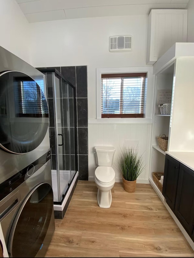 bathroom with stacked washing maching and dryer, hardwood / wood-style floors, vanity, walk in shower, and toilet