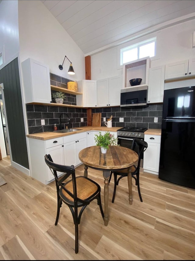 kitchen featuring vaulted ceiling, butcher block countertops, sink, white cabinets, and stainless steel appliances