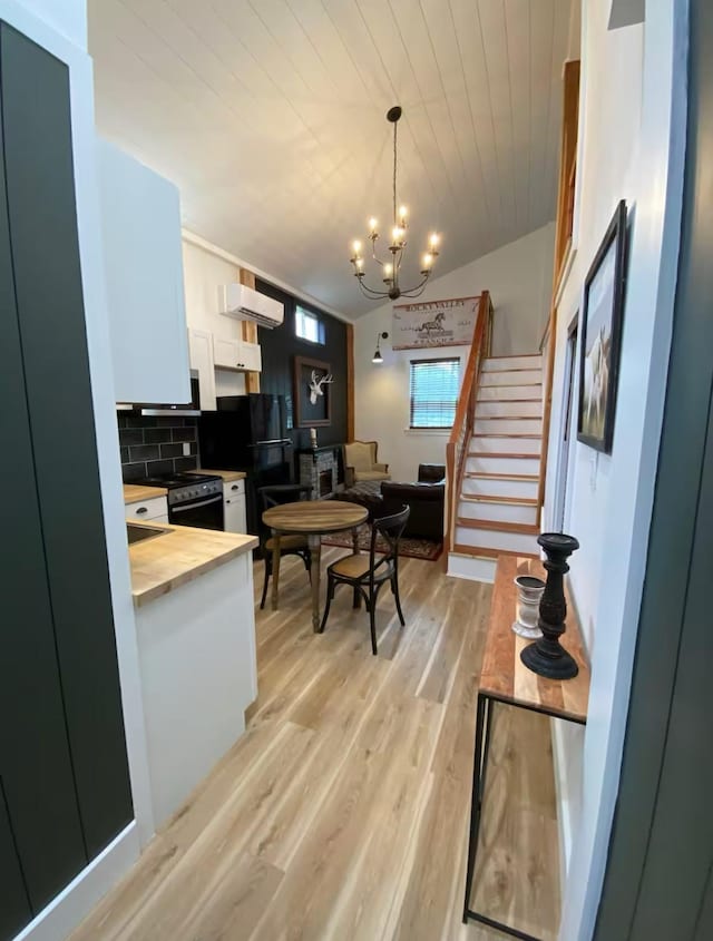 kitchen with black refrigerator, tasteful backsplash, white cabinets, decorative light fixtures, and light wood-type flooring