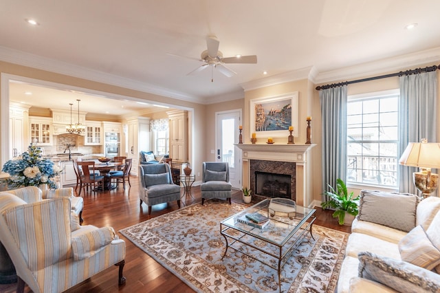 living room with ceiling fan with notable chandelier, a fireplace, ornamental molding, and dark hardwood / wood-style floors