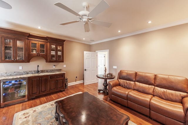 living room featuring wine cooler, crown molding, indoor wet bar, light wood-type flooring, and ceiling fan