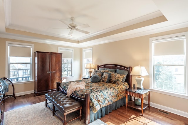 bedroom featuring crown molding, wood-type flooring, a tray ceiling, and multiple windows