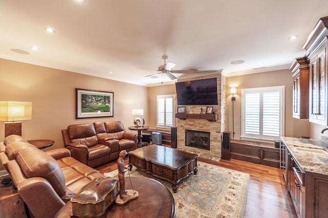 living room featuring sink, crown molding, ceiling fan, a fireplace, and light hardwood / wood-style floors