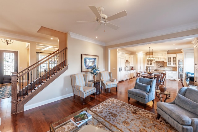 living room with dark wood-type flooring, ornamental molding, sink, and ceiling fan with notable chandelier