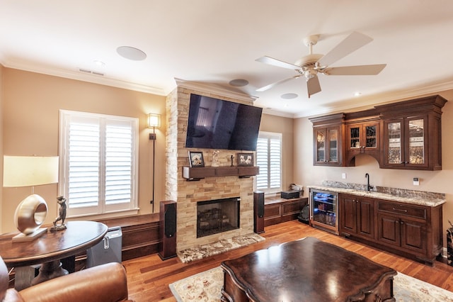 living room with indoor bar, a large fireplace, beverage cooler, ornamental molding, and light wood-type flooring