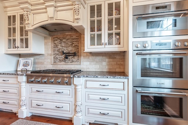 kitchen featuring stainless steel appliances, premium range hood, tasteful backsplash, and stone counters