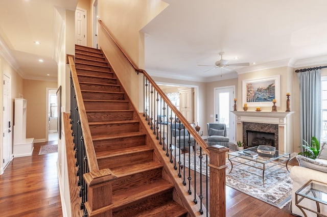 stairs with crown molding, ceiling fan, a fireplace, and hardwood / wood-style floors