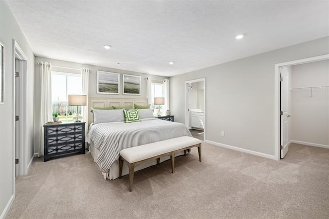 bedroom featuring ensuite bath, a walk in closet, light colored carpet, a textured ceiling, and a closet