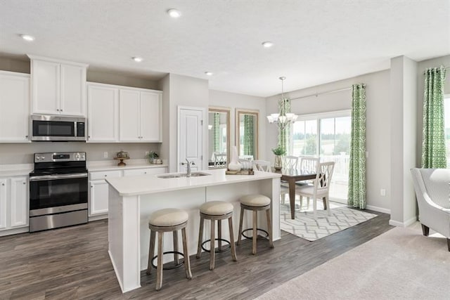 kitchen with sink, appliances with stainless steel finishes, hanging light fixtures, an island with sink, and white cabinets