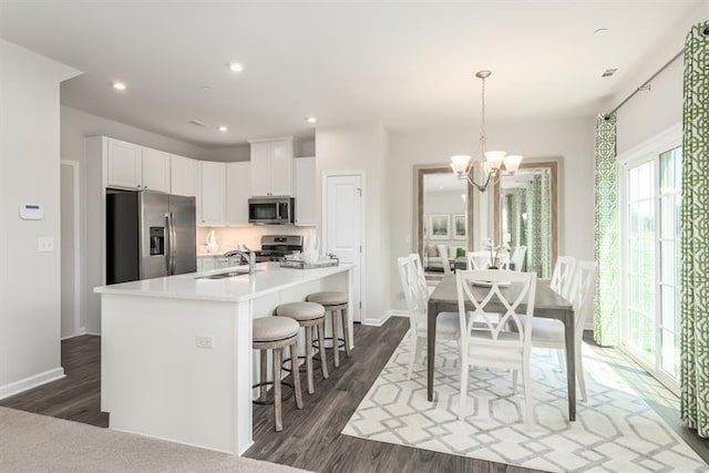 kitchen with white cabinetry, hanging light fixtures, dark hardwood / wood-style floors, stainless steel appliances, and a kitchen island with sink