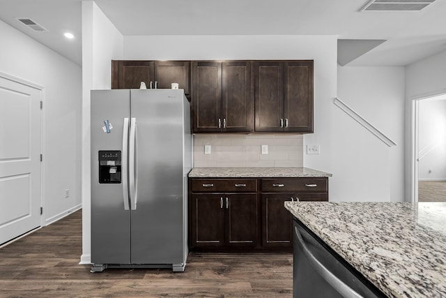 kitchen featuring light stone counters, dark brown cabinets, dark hardwood / wood-style floors, stainless steel fridge, and backsplash