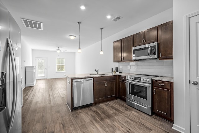 kitchen with appliances with stainless steel finishes, sink, hanging light fixtures, kitchen peninsula, and dark wood-type flooring