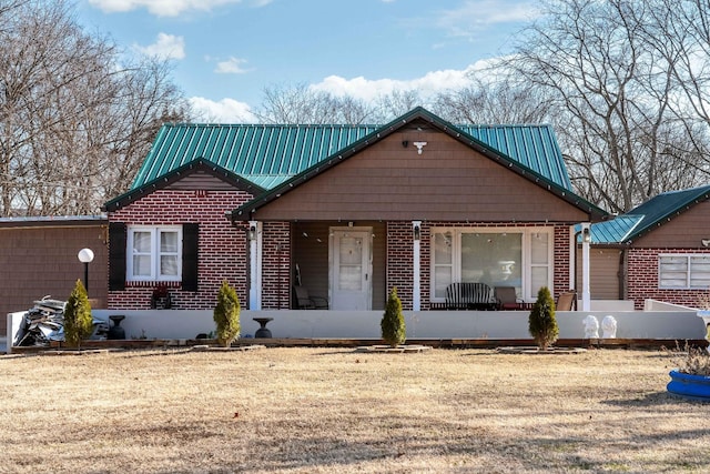 view of front of property with a porch, brick siding, a front yard, and metal roof