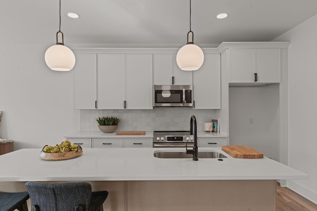 kitchen with pendant lighting, appliances with stainless steel finishes, sink, and a center island with sink