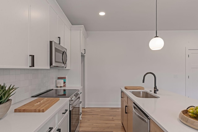 kitchen with sink, tasteful backsplash, decorative light fixtures, stainless steel appliances, and white cabinets